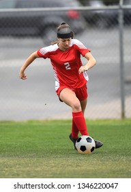High School girl playing soccer, kicking the ball.