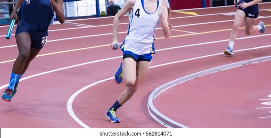 High School Girls Running In A Relay Race On A Banked Track, Indoors.