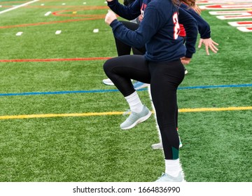 High School Girls Track And Field Team Perfoming The Speed Drill A-Skip In A Straight Line On A Green Turf Field.