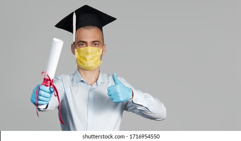 High School Graduation During A Quarantine. Student Graduate In A Hat And A Protective Mask Holds A Diploma And Shows Thumb Up