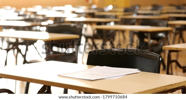 A high school hall or room set up ready\
for an end of year final exam to be sat by students. examination\
paper sitting on the edge of a desk or table.\
