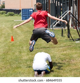 A High School Kid Plays Leapfrog Behind The Bleachers On The Grass At The End Of Practice