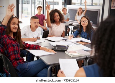 High school kids raise hands, teacher sitting at their desk