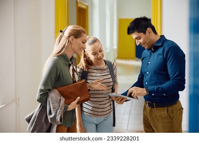 High school principal using digital tablet during a meeting with female student and her mother in hallway.