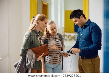 High school principal using digital tablet during a meeting with female student and her mother in hallway.