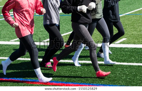 A high\
school running team is running together wearing spandex and socks\
with long sleeves due to cold\
weather.