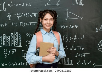 A high school schoolgirl stands near the blackboard with a textbook her hands, portrait of a teenage girl at school. - Powered by Shutterstock