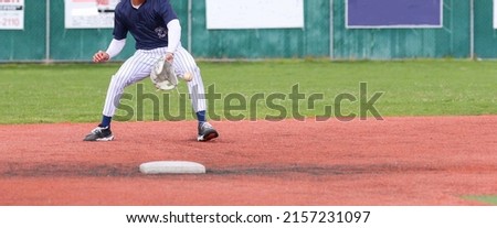 High school second baseman backhands a ground ball into his white baseball glove making the play during a game.