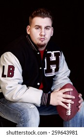 High School Senior Posing With Football While Wearing Championship Jacket With Letter H And LB For Linebacker