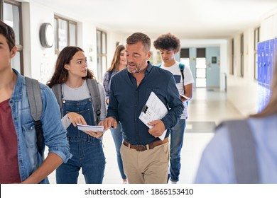 High school student asking doubt to professor. Mature man professor answering to girl in university campus. High school lecturer talking to schoolgirl at the end of the lesson while walking in hallway
