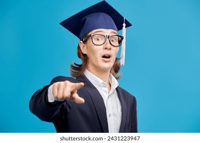 A high school student boy in a suit and glasses is very surprised. Studio blue background. Education. Copy space.