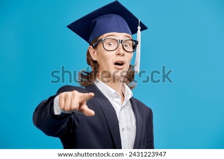 A high school student boy in a suit and glasses is very surprised. Studio blue background. Education. Copy space.