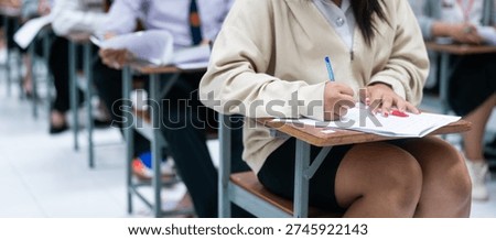 High school student concentrating while writing answers on exam paper in classroom.