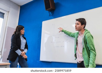 High school student explaining a math formula on a whiteboard to his teacher during a class