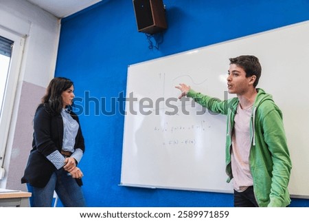 High school student explaining a math formula on a whiteboard to his teacher during a class