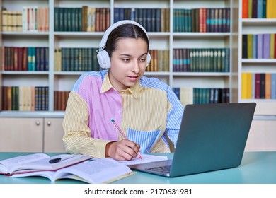 High School Student Girl In Headphones Studying In School Library Using Books And Laptop