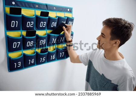 High school student leaving his smart phone in cell phone organizer on the wall before entering the classroom at school.