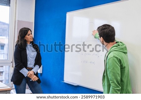 High school student solving a math equation on the whiteboard while the teacher watches during a class