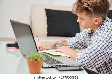 High School Student Studying At Home During Lockdown And Writing Essay In Textbook