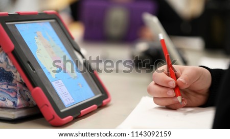 High school student using electronic device tablet style computer research learning knowledge. Theme of classroom teaching teacher pedagogy educate and education  modern contemporary learning tools.