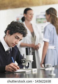 High School Student Using Microscope And Taking Notes In Laboratory