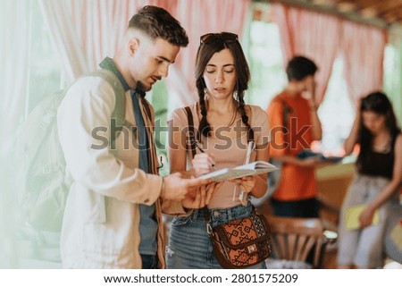 High school students collaborate as one signs a notebook while another reviews notes. A small group of teenagers converse and study together in a relaxed indoor school environment.
