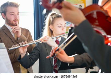 High School Students Playing Flute And Violin In A Music Class With Their Teacher Watching Them.