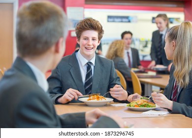 High School Students In Uniforms Eating Lunch At The Cafeteria.