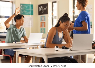 In high school, students using laptops and writing in classroom, teacher assisting. Education, learning, technology, studying, teaching, digital
