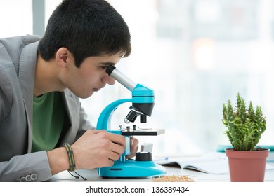 High School Students. Young Handsome Male Student Looking Through Microscope Biological Sample In Science Classroom
