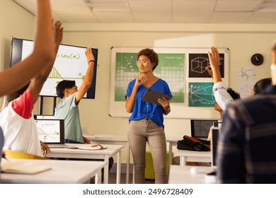 In high school, teacher holding tablet and engaging students raising hands in classroom. Education, teaching, learning, technology, engagement, interaction - Powered by Shutterstock