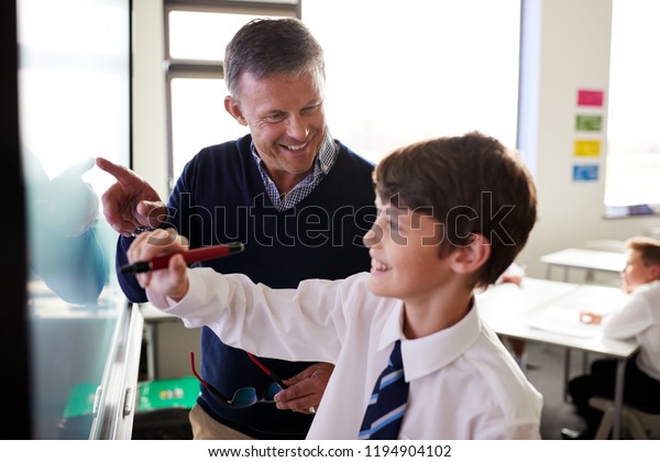 High School Teacher With Male\
Student Wearing Uniform Using Interactive Whiteboard During\
Lesson