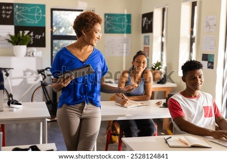 In high school, teacher using tablet while engaging with students in classroom. Education, technology, learning, interaction, digital, instructing