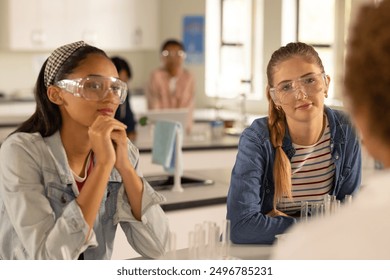 In high school, teenage girls wearing safety goggles listening in science class. Education, classroom, learning, experiment, laboratory, teaching - Powered by Shutterstock