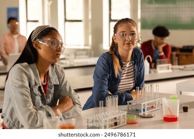 In high school, teenage girls wearing safety goggles attending chemistry class. Education, learning, classroom, science, experiment, laboratory - Powered by Shutterstock