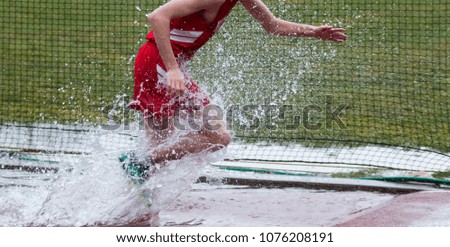 A high school track and field runner competing in the steeplechase running, splashing, out of the water.