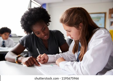 High School Tutor Giving Female Student Wearing Uniform One To One Tuition At Desk