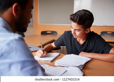 High School Tutor Giving Male Student One To One Tuition At Desk