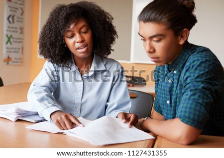 High School Tutor Giving Male Student One To One Tuition At Desk