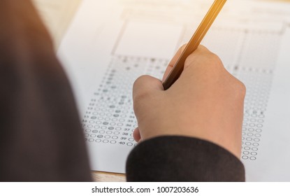 High School Or University Student Hands Taking Exams, Writing Examination On Paper Answer Sheet Optical Form Of Standardized Test On Desk Doing Final Exam In Classroom. Education  Literacy Concept.