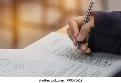 High School Or University Student Hands Taking Exams, Writing Examination On Paper Answer Sheet Optical Form Of Standardized Test On Desk Doing Final Exam In Classroom. Education  Literacy Concept.