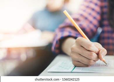 high school or university student holding pencil writing on paper answer sheet.sitting on lecture chair taking final exam attending in examination room or classroom.student in uniform