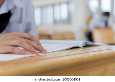 High School Or University Student Reading Question Exam Test And Using Pencil Writing On Paper Answer Sheet, Doing Final Exam Attending In Examination Classroomwith Student In Uniform