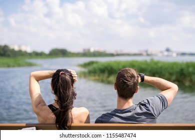 High section back view of young couple sitting on bench enjoying lake view in park, copy space