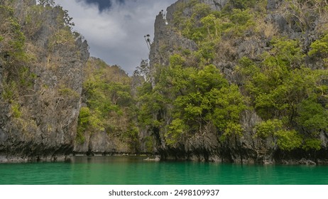 High sheer karst cliffs surround the emerald lagoon. Green tropical trees on steep slopes. Tourist canoes float in the bay. Blue sky, clouds. Philippines. Palawan. Small Lagoon. The Bacuit archipelago - Powered by Shutterstock