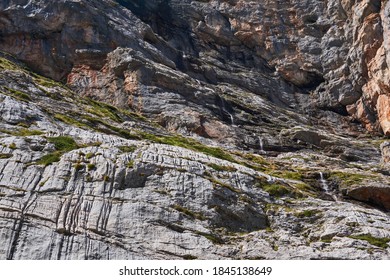 High Sheer Rock Wall With A Small Waterfall Flowing Down It