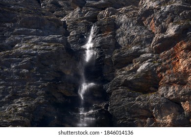 High Sheer Rock Wall With A Small Waterfall Flowing Down It