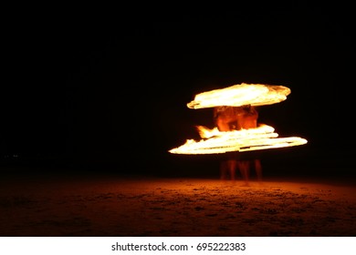 High Skill two Men playing fireworks by spinning wood pole top bottom, circle around as ring of fire on beach along ocean in tropical island, long high exposure blur movement