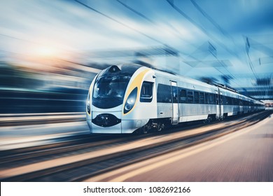 High speed passenger train in motion on the railway station at sunset in Europe. Modern intercity train on railway platform with motion blur effect. Urban scene with railroad. Railway transportation - Shutterstock ID 1082692166