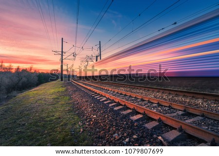 High speed passenger train in motion on railroad at sunset. Blurred modern commuter train. Railway station and colorful sky. Railroad travel, railway tourism. Industrial landscape. Transportation